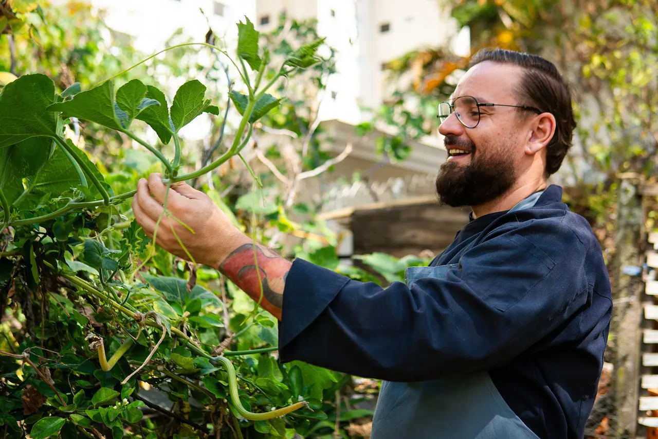 Chef Henrique colhendo folhas na horta